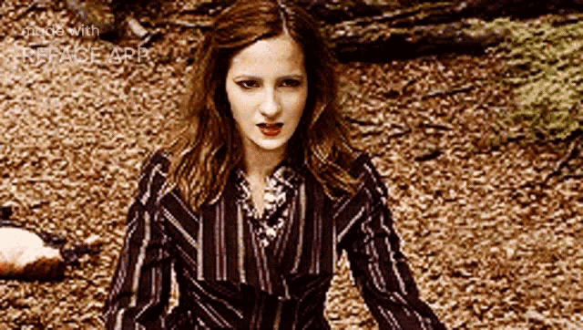 a woman in a striped shirt is sitting in a pile of leaves in the woods .