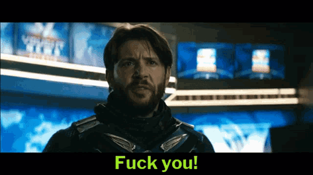a man with a beard is standing in front of a screen that says " fuck you "