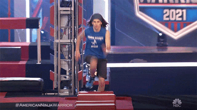 a man in a blue tank top is jumping over a red box on a stage with the year 2021 on it