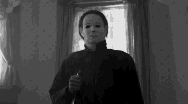 a man in a mask is holding a knife in a room .