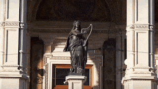 a statue of a woman holding a harp in front of a building with columns