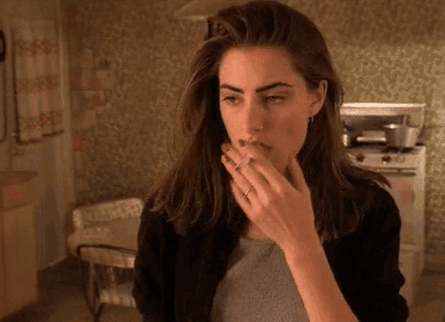 a woman is smoking a cigarette in a kitchen while wearing a ring on her finger