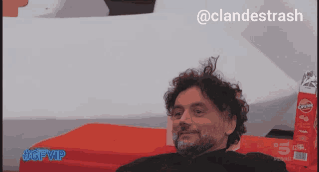 a man with curly hair sits in front of a box of chips with the hashtag #gfvip