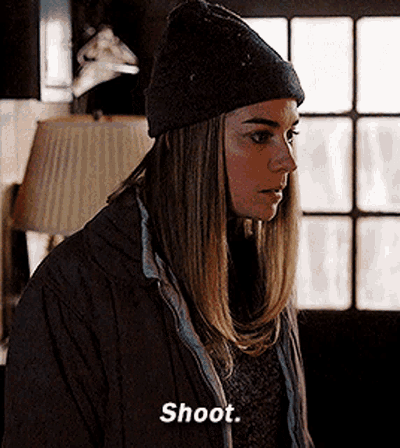 a woman wearing a beanie and a jacket says " shoot "