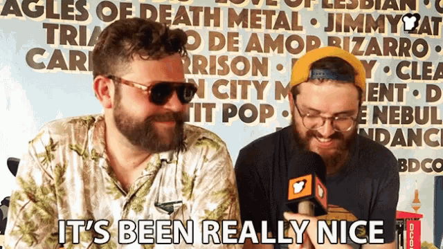 two men are sitting in front of a sign that says ' it 's been really nice '
