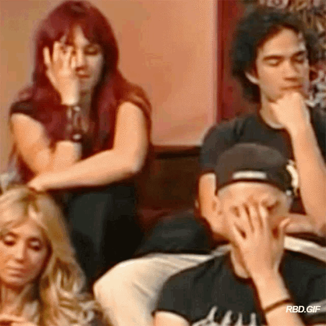 a group of people are sitting in a room and one of them is covering his face with his hands