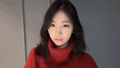 a young woman wearing a red turtleneck sweater and earrings looks at the camera .