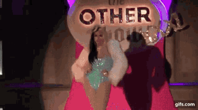 a drag queen is standing in front of a sign that says other world .