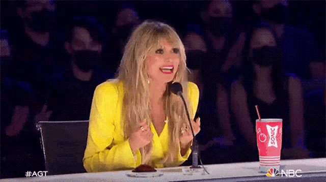 a woman in a yellow jacket is sitting in front of a microphone with a red cup of coca cola in front of her .