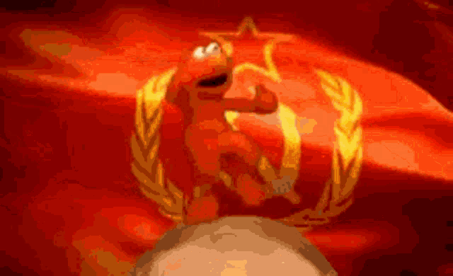 elmo is standing on a rock in front of a red flag with a star and laurel wreath .