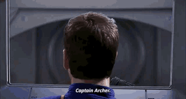 a man in a blue shirt is looking out of a window and talking to captain archer .