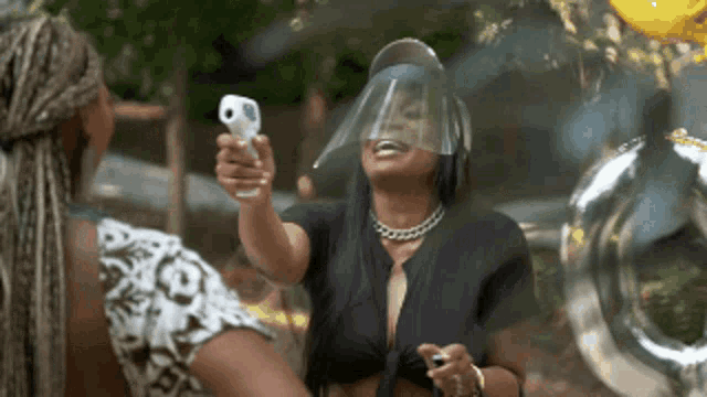 a woman wearing a face shield is holding a thermometer to her face .