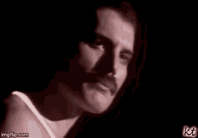 a close up of a man 's face in a dark room with a white tank top on .