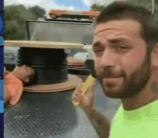 a man with a beard is standing next to a spool of wire and eating a banana .