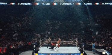 a wrestler in red , white and blue pants is holding a rope in a ring .