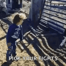 a young boy is standing in the dirt in front of a fence and a bull .