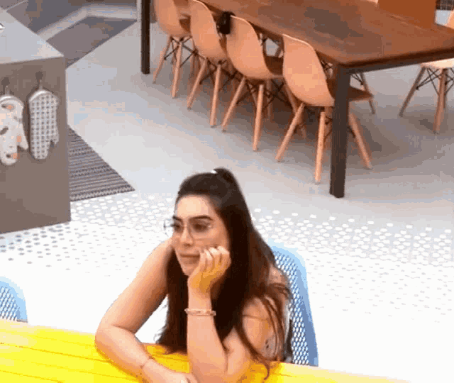 a woman wearing glasses sits at a yellow table in a kitchen