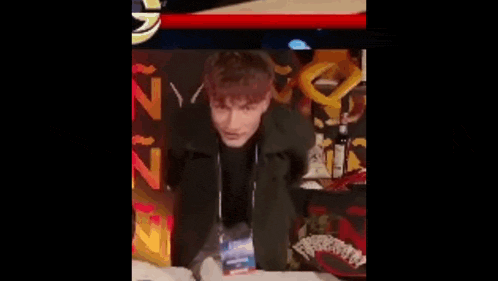 a man in a black jacket is sitting in front of a sign that says ninjago on it .