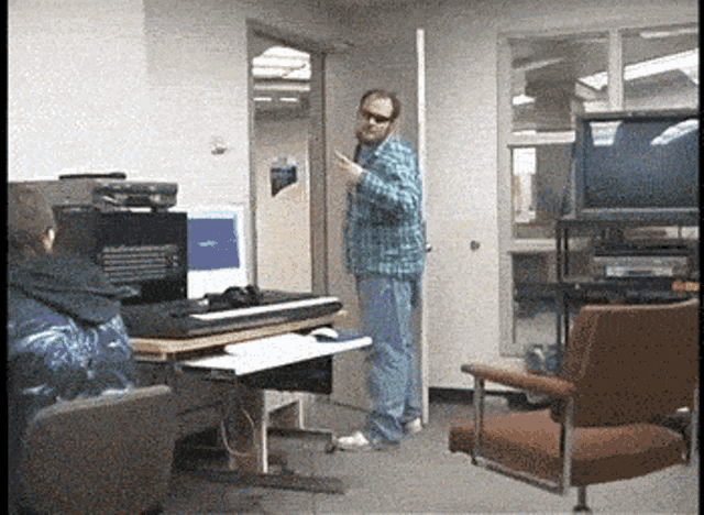 a man in a plaid shirt is standing in front of a computer in a room