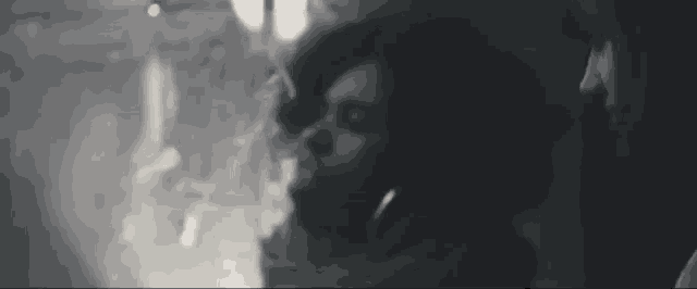 a black and white photo of a woman smoking a cigarette while looking out a window .