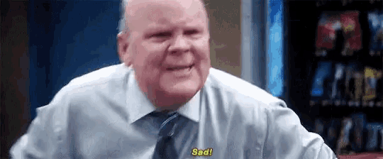 a man in a suit and tie is smiling and saying `` sad '' while standing in front of a vending machine .