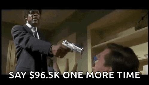 a man in a suit is pointing a gun at another man and saying `` say $ 96.5k one more time '' .