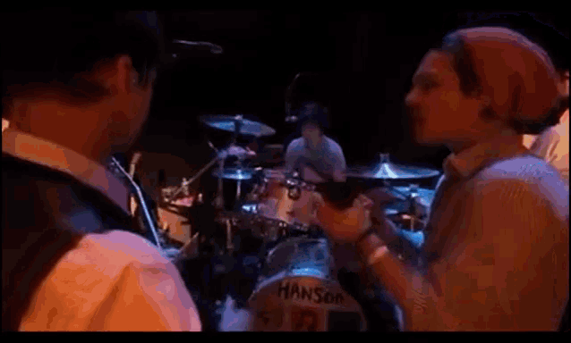 a man in a red hat stands in front of a drum set that says hanson