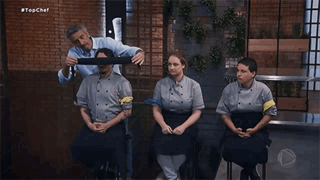 a man is covering a man 's eyes with a bandage while a group of chefs sit in a row .