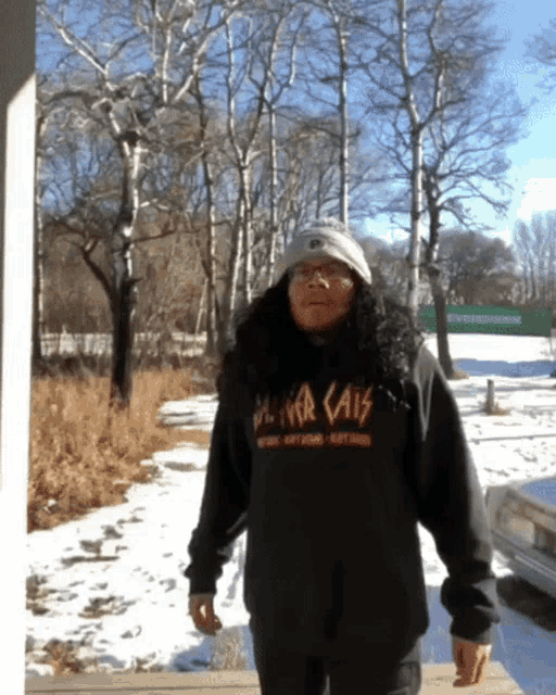 a man wearing a black hoodie with the word cats on it stands in the snow