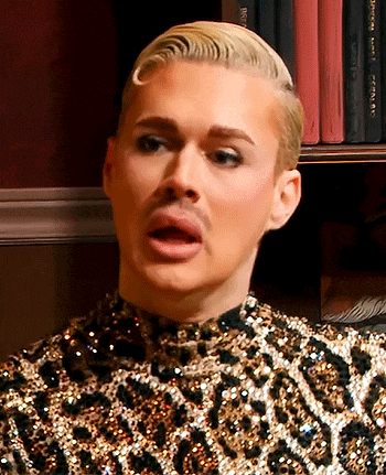a man wearing a leopard print top looks at the camera with his mouth open