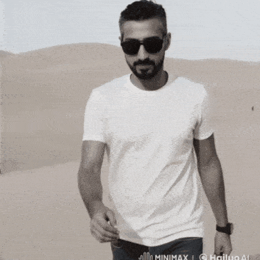 a man wearing sunglasses and a white t-shirt is walking through a desert