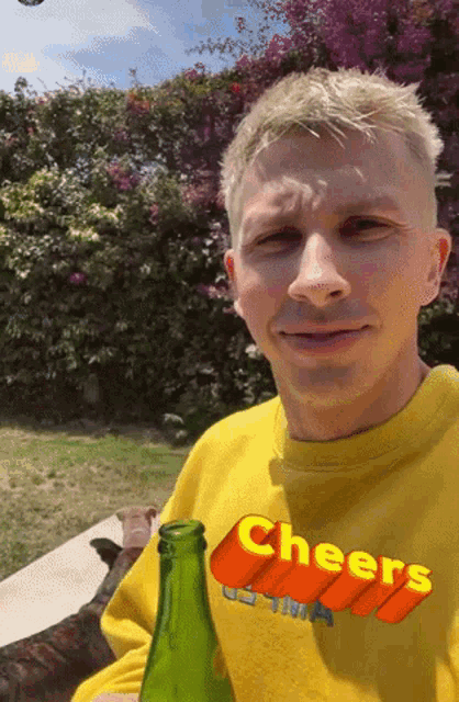 a man wearing a yellow shirt that says cheers holds a green bottle