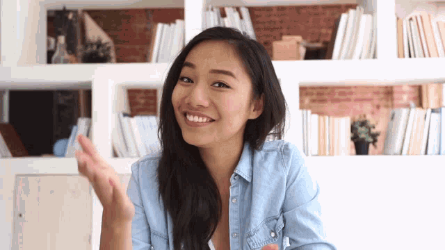 a woman in a blue shirt is smiling in front of book shelves