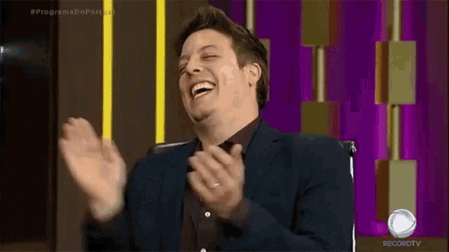 a man in a suit is laughing and clapping in front of a recordtv sign