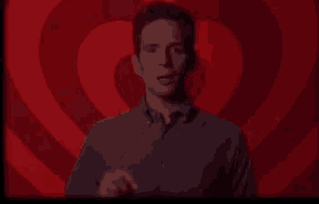 a man in a blue shirt is pointing up in front of a red heart .