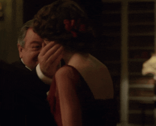 a man in a tuxedo is touching the back of a woman 's head