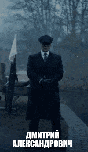 a man in a suit and hat is standing in front of a flag with the name dmitryi alexandrovich written on the bottom
