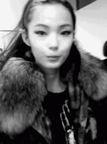 a woman is wearing a fur coat and making a funny face in a black and white photo .