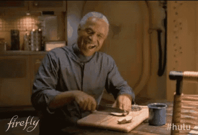 a man is sitting at a table cutting food on a cutting board and smiling .