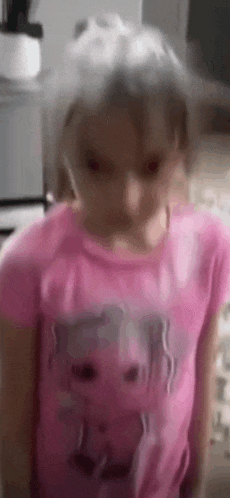 a little girl is wearing a pink shirt with a cat on it and making a funny face .