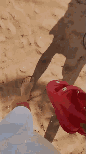 a person 's foot is on the sand next to a red kayak with the letters cc on it