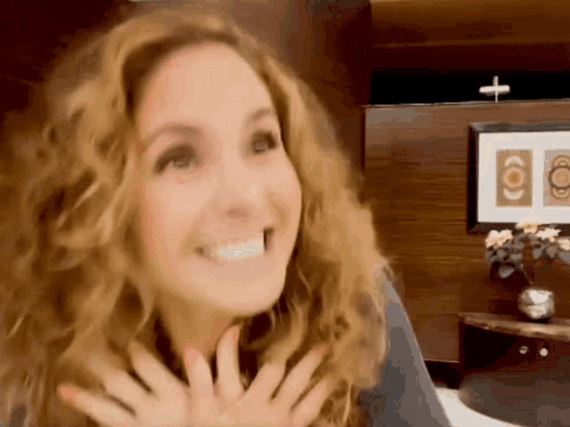 a woman with curly hair is smiling in front of a picture of a cross