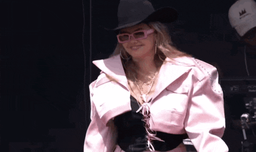 a woman wearing a cowboy hat and pink sunglasses is smiling