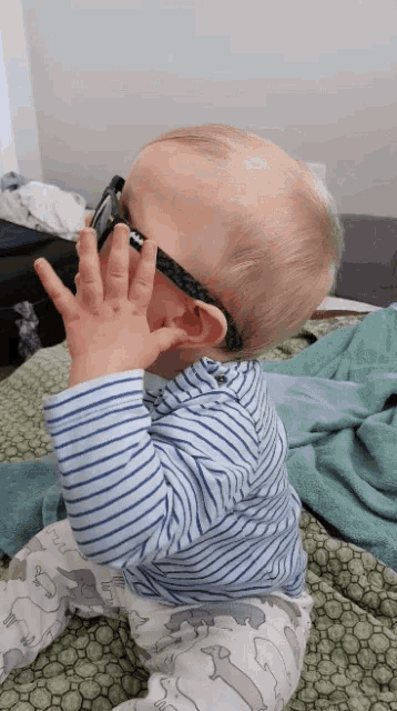 a baby wearing sunglasses and a striped shirt is laying on a bed