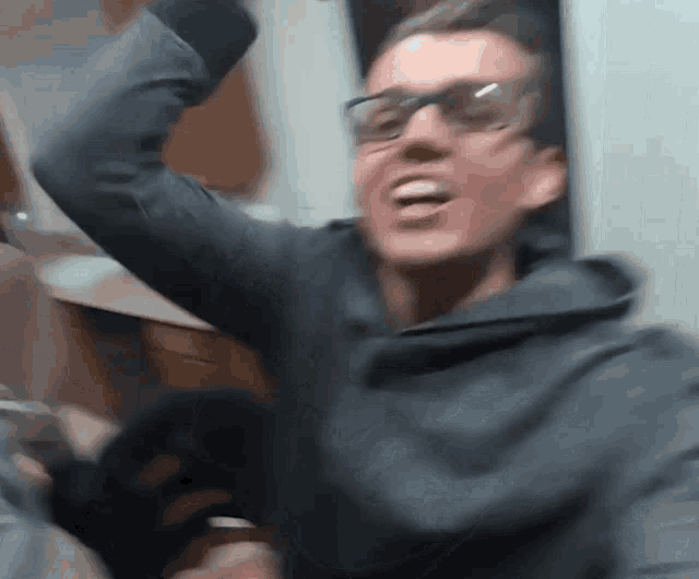 a man wearing glasses and a hoodie is laughing with his hands in the air