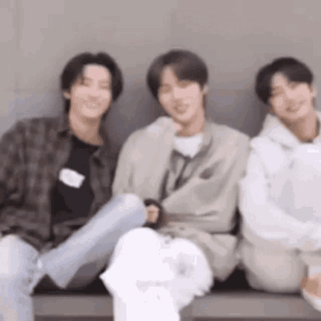 a group of three young men are sitting next to each other on a bench .