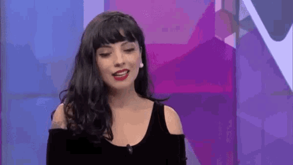 a woman with long black hair and red lipstick is standing in front of a purple wall .