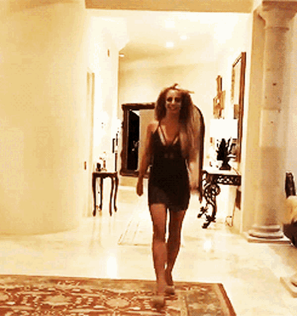a woman in a black dress walks through a hallway