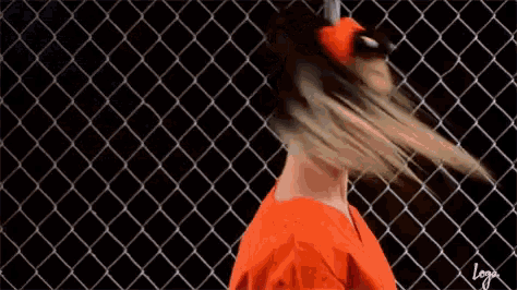 a woman in a red shirt and headband is standing in front of a chain link fence .