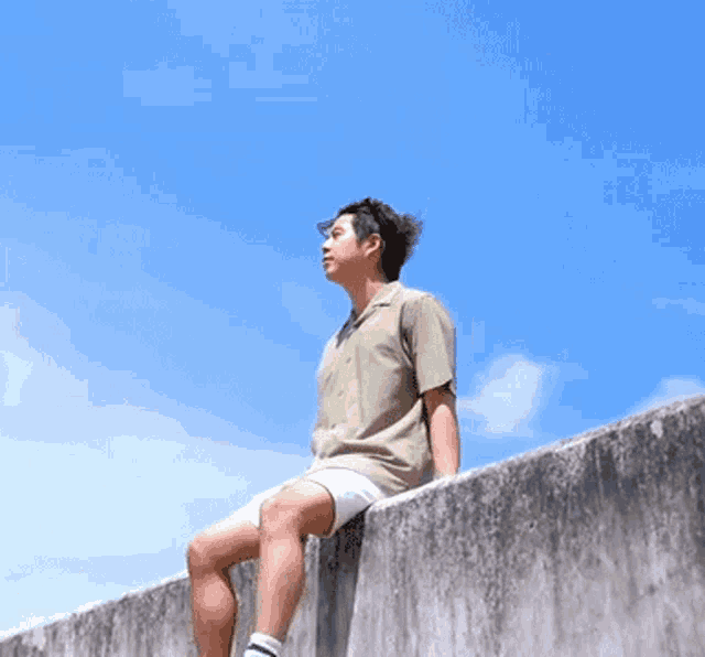 a man in a green shirt and white shorts is sitting on a wall